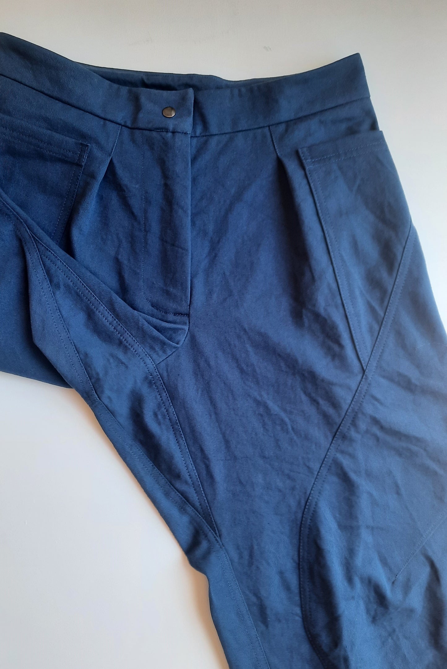 A pair of blue pants laid flat with seam detailing across the front of the leg with a gusseted crotch
