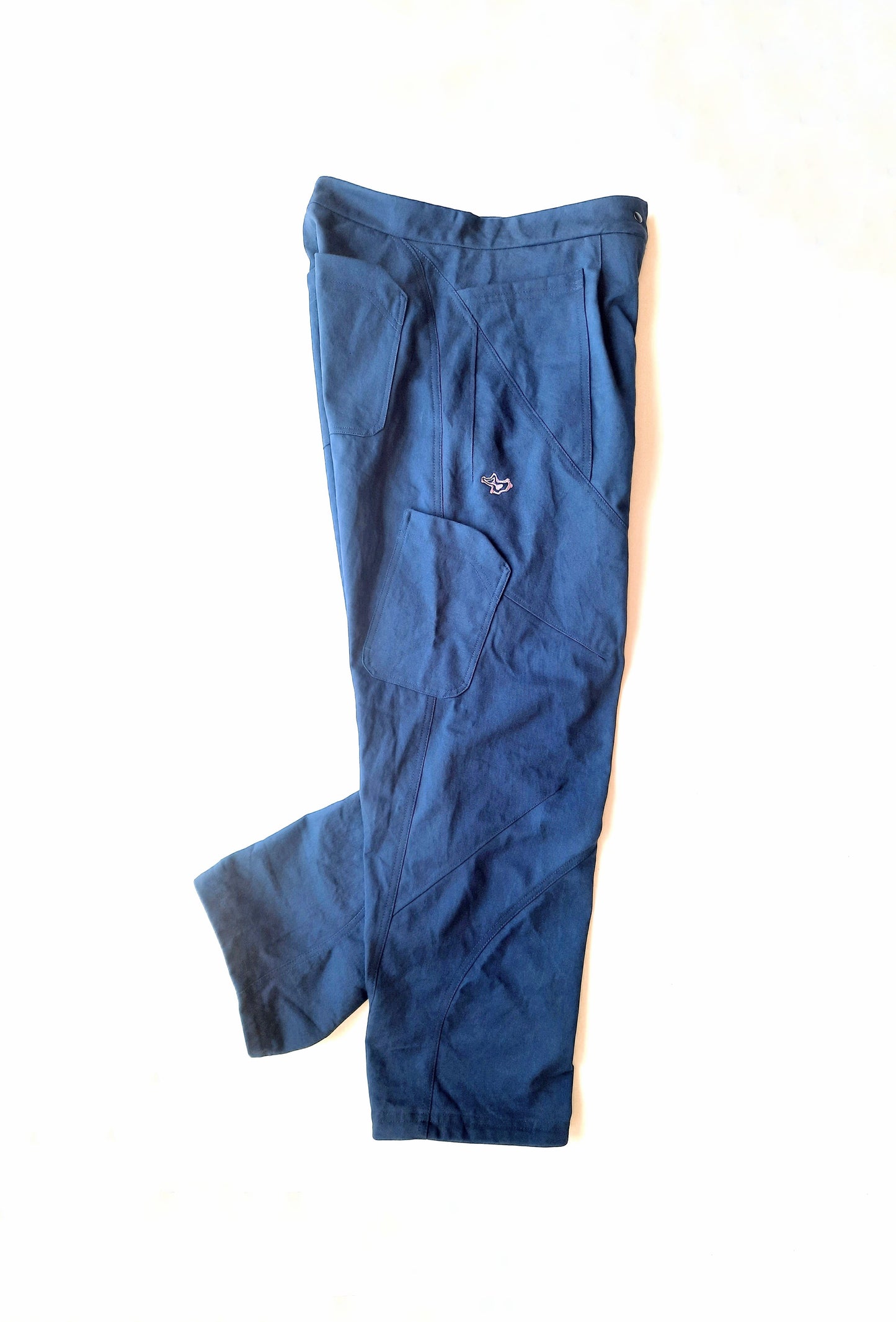 A flat lay photo of a blue pair of pants with front, back and side pockets with a purple logo