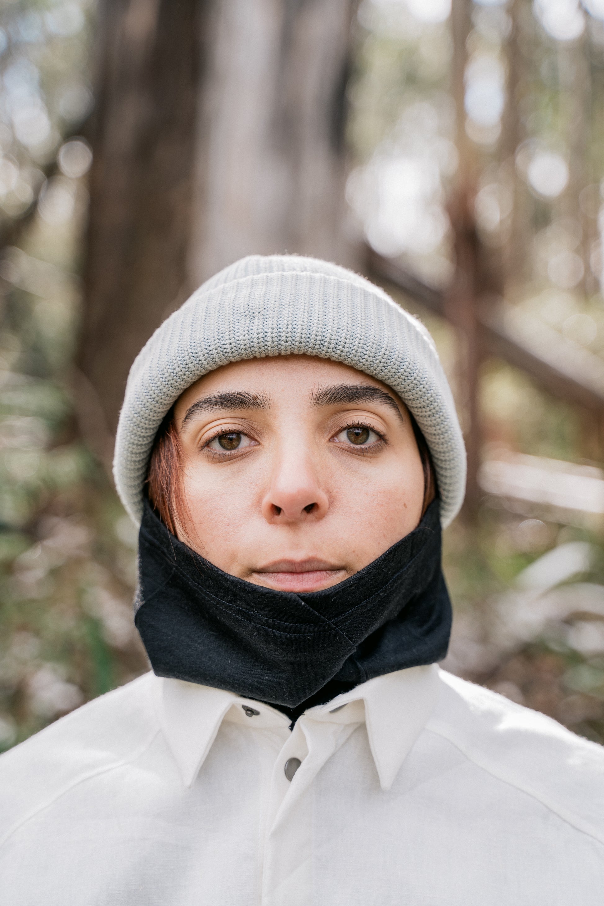 A womans head pictured with a white beanie and black neck tube facing towards the camera