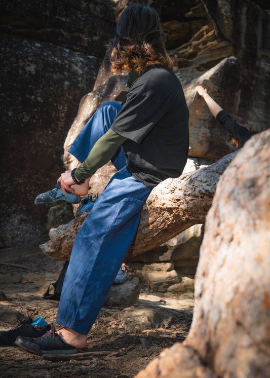 a girl sitting on a rock putting bouldering shoes on