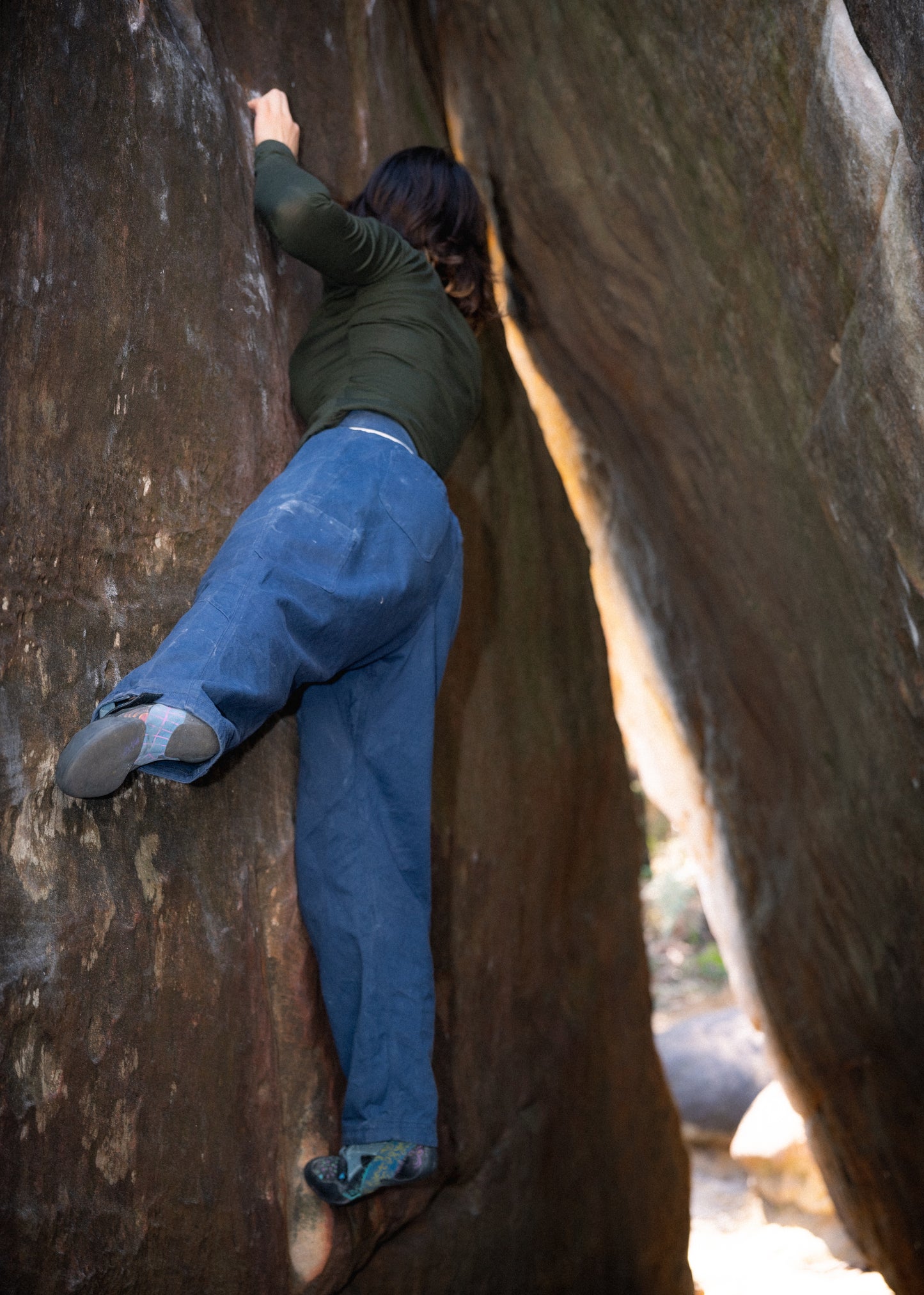 A woman bouldering in a green shirt and blue pants