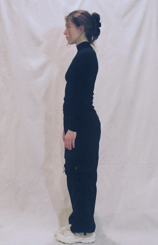 A photo of a girl standing in front of a white background wearing a black long sleeve shirt standing side on to the camera.