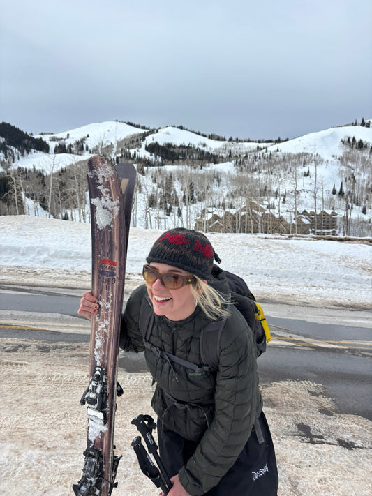 a girl holding skis wearing a beanie in a snowy landscape