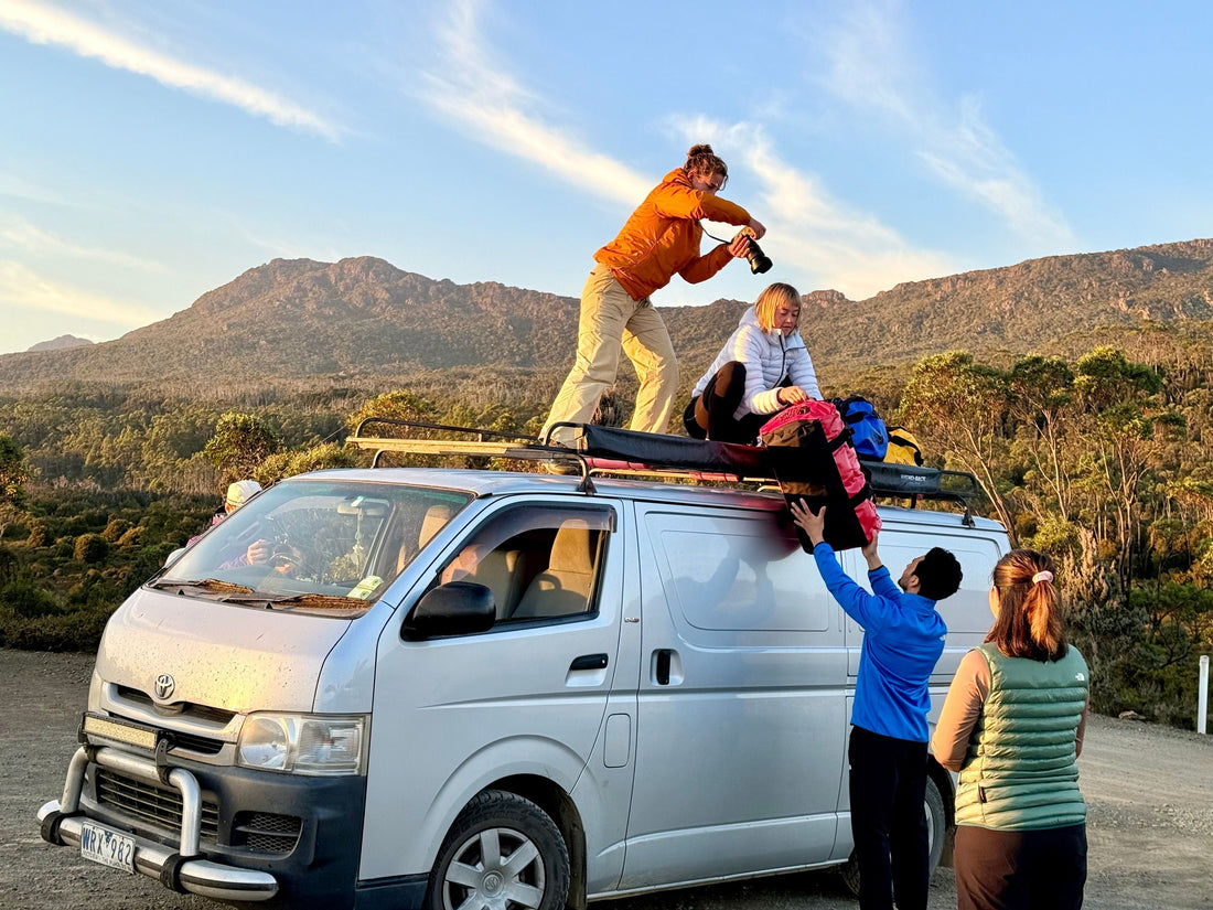 A woman standing on top of a vehicle taking photos of adventure gear