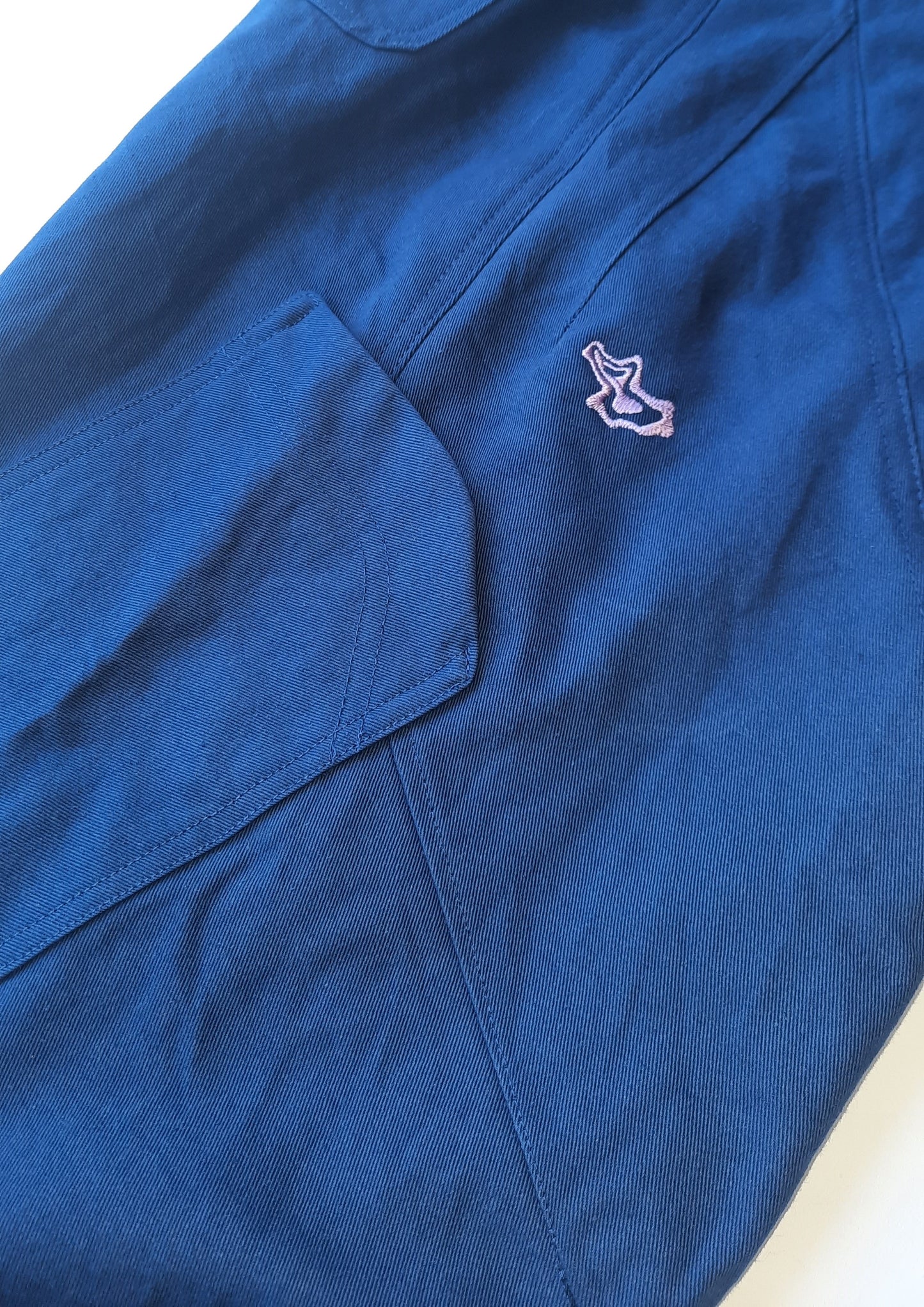 A detailed photo of a blue pant leg with a purple logo and pocket on the side of the pant