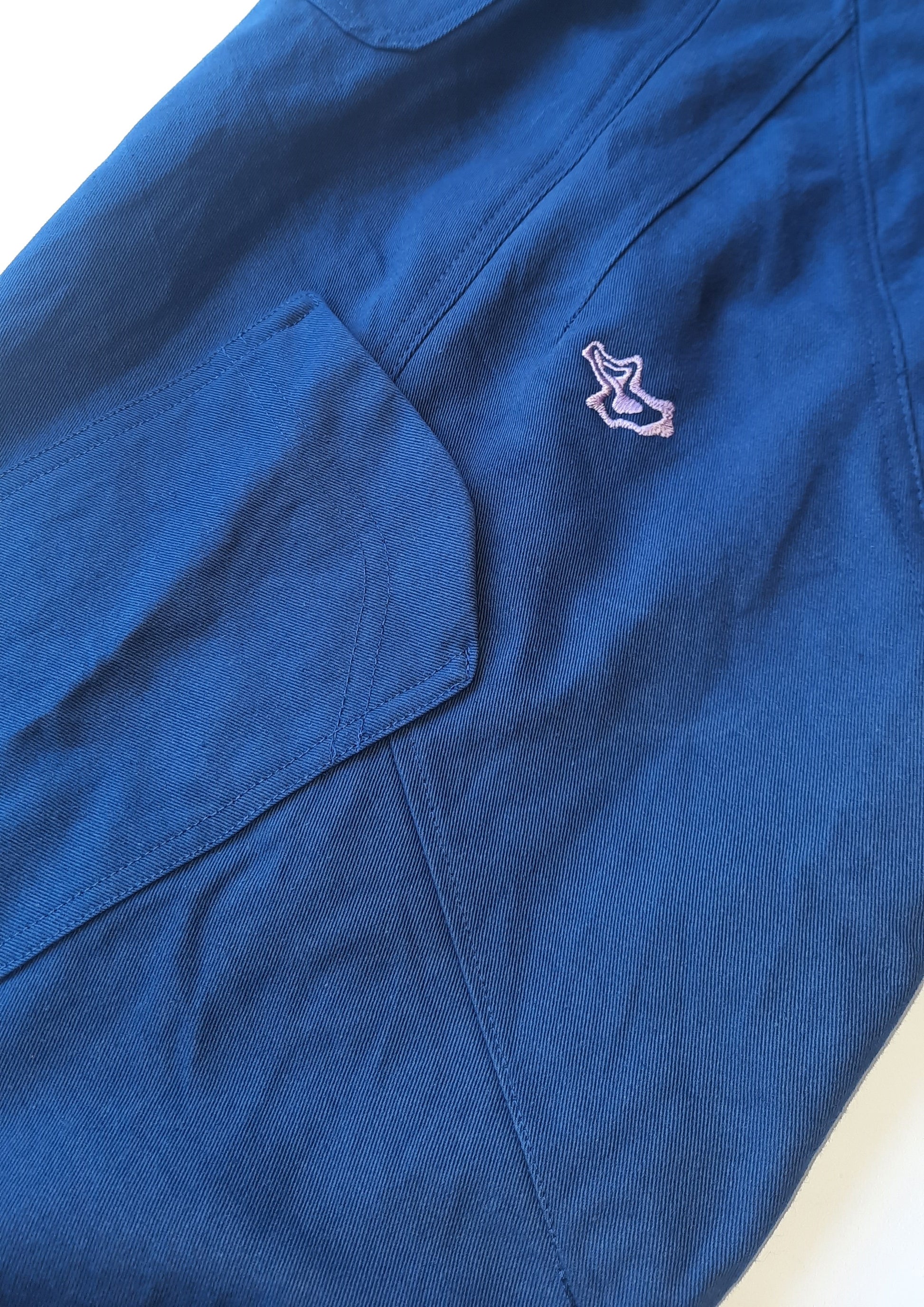 A detailed photo of a blue pant leg with a purple logo and pocket on the side of the pant