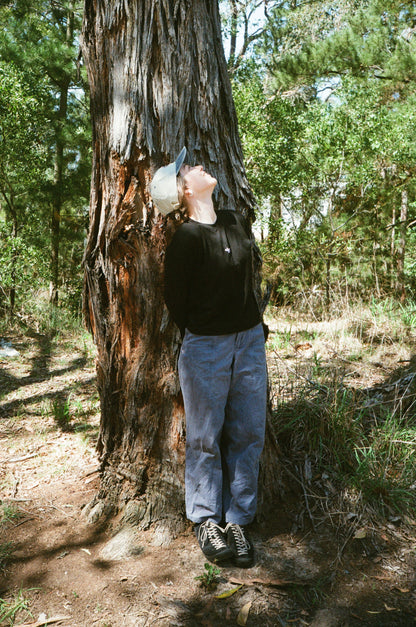 A woman standing against a tree wearing a black shirt and blue pants