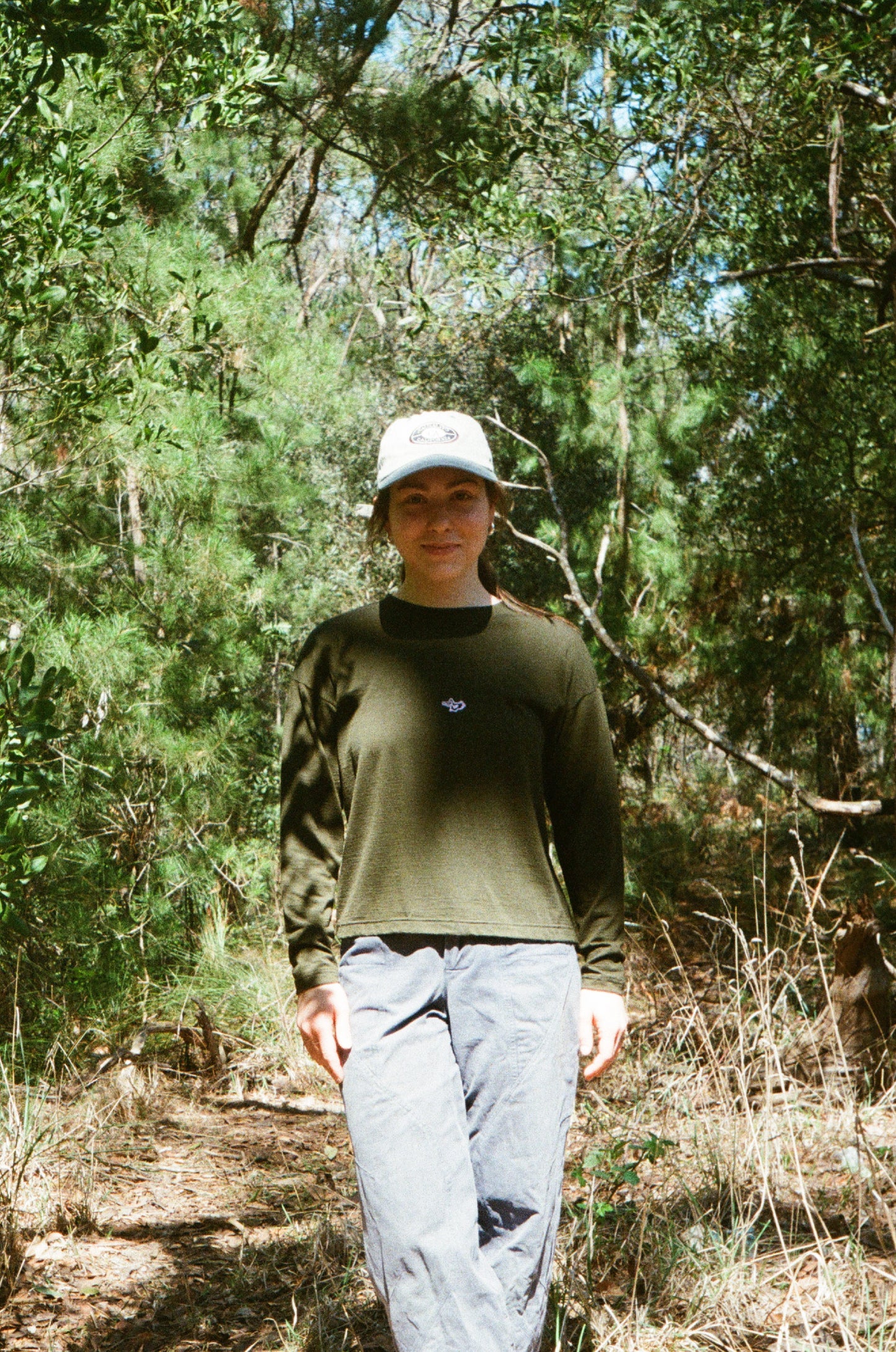 A woman wearing an olive tee and a hat in some trees