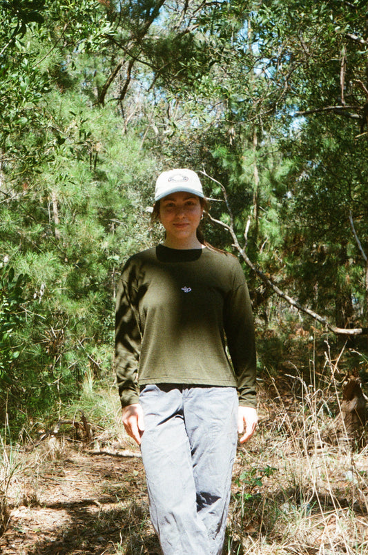 A woman wearing an olive tee and a hat in some trees