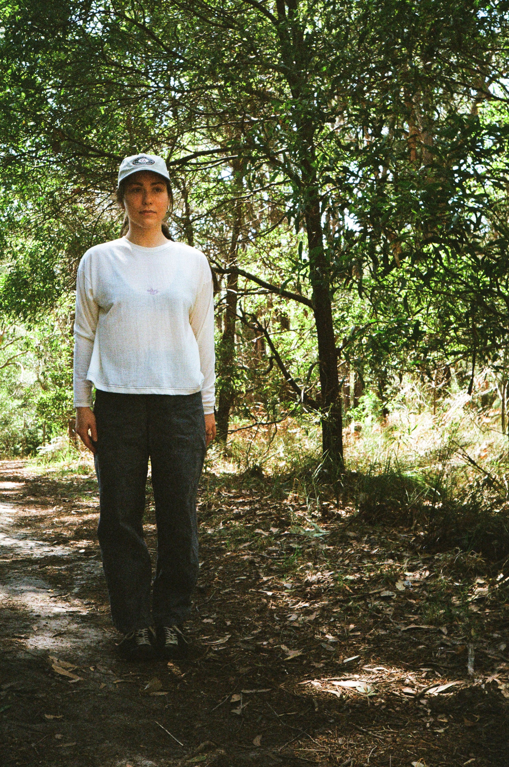 A woman standing in some trees wearing a white shirt and blue pants