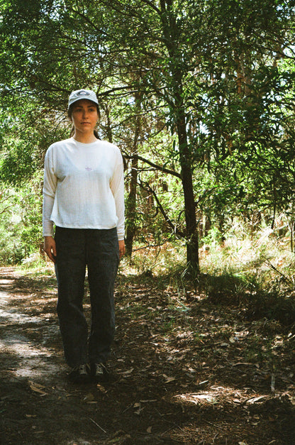 A woman standing in some trees wearing a white shirt and blue pants