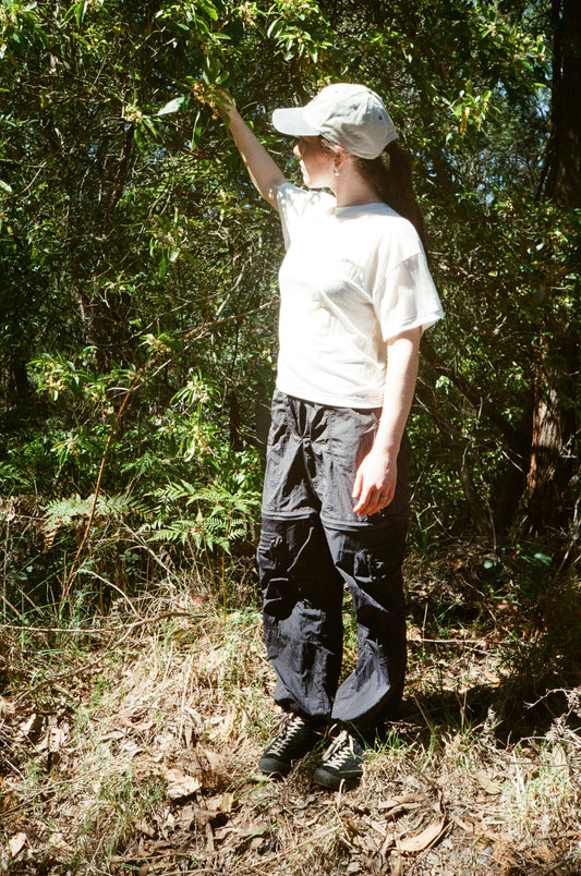 A woman inspecting some leaves wearing a white shirt and black pants