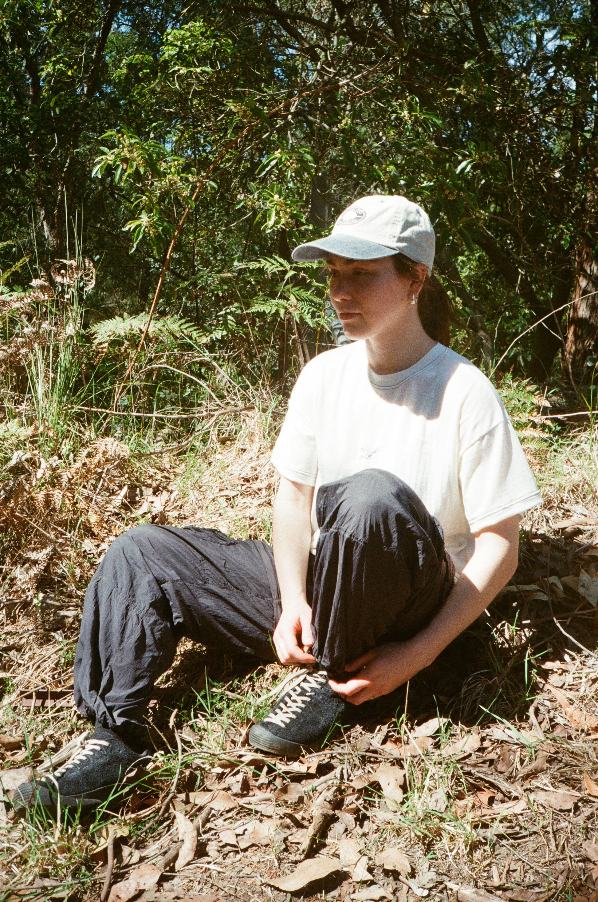 A woman sitting in a white shirt and black pants in the grass