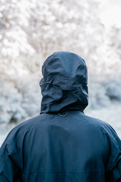 A man standing facing away from the camera with the hood of a jacket up.