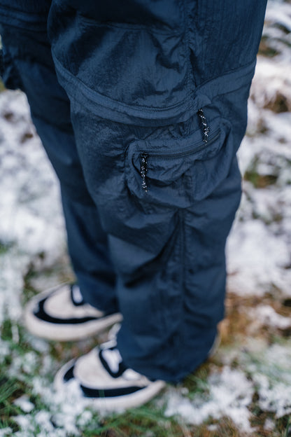 A mans legs pictured with long black pants.  Focussing on the detail of the zip off pant and pocket on the side of the pant.