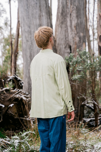 A man wearing blue pants and a green shirt standing in front of some large gum trees facing away from the camera.