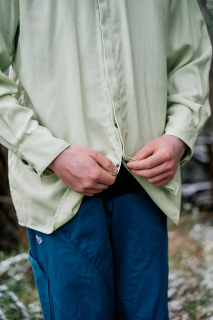An image of a man buttoning up a green shirt that has snaps.