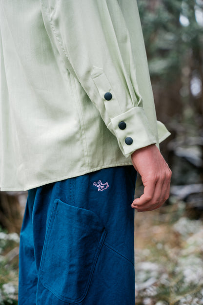 An image of  a mans arm and blue pants.  The shirt is green and has three snaps on the cuff.
