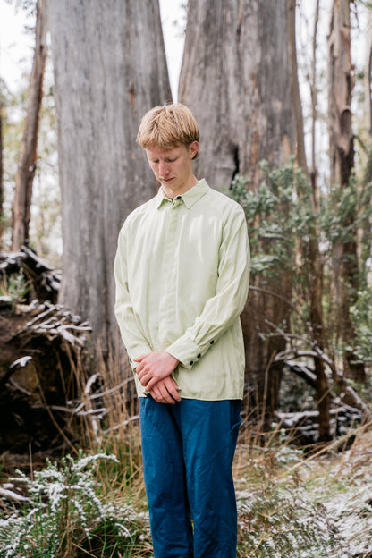 A man wearing blue pants and a green shirt standing in front of some large gum trees. 