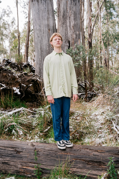 A man wearing blue pants and a green shirt standing in front of some large gum trees. 