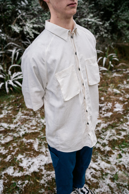 A man in a white shirt and blue pants standing in snow covered bush facing towards the side.