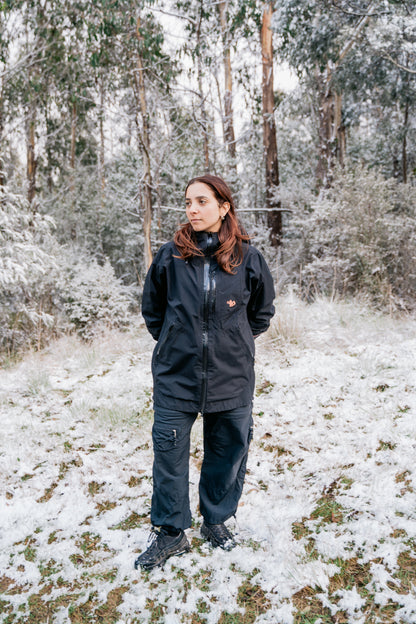 A woman wearing a black jacket and black pants, standing in a snowy landscape facing the camera.