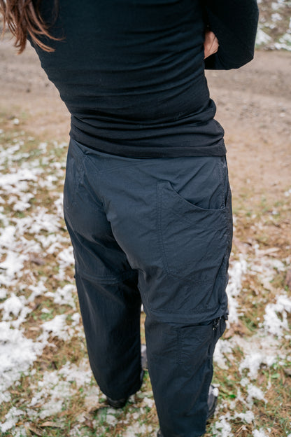 A woman pictured from the top angling down to capture the back pocket details of a black pair of pants