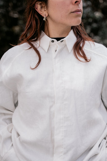 A woman standing in a white shirt with the first button on the collar undone.