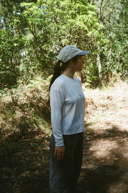 A woman standing in a white shirt wearing a hat in some trees
