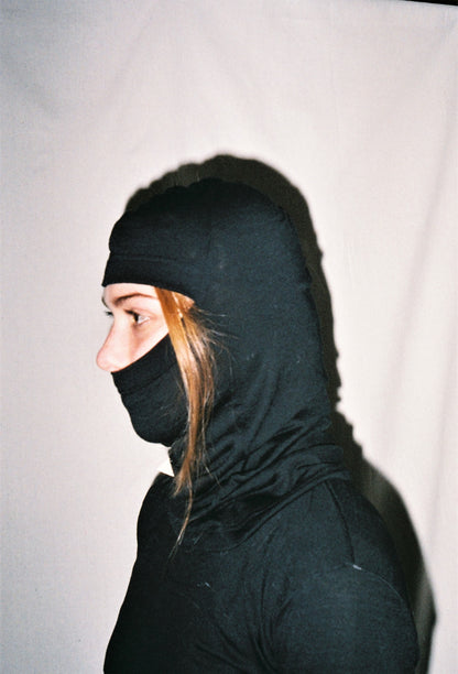 A side view image of a girl wearing a black balaclava with a strand of hair coming out from the front of the balaclava opening.