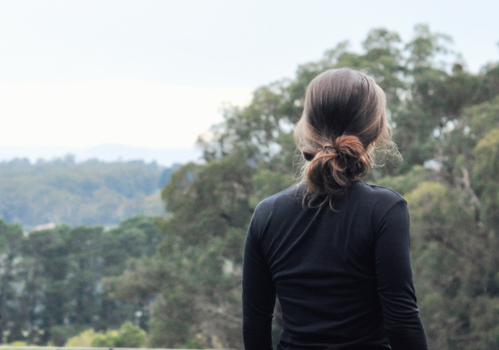 An image of a girl standing outside with trees in the background wearing a black long sleeve shirt