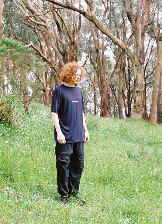 A photo of a man standing in lush grass and trees wearing black pants and a navy shirt