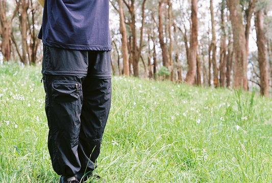 An image of a person wearing black zip off pants in lush grass.