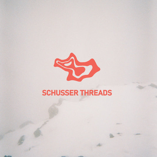 Schusser Threads logo and text on top of a misty snowy background.